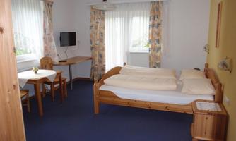 A cozy bedroom with a double bed, a table, and chairs. Light curtains let in a lot of light.