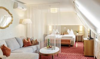 An elegant hotel room with a cozy sofa and a round table. The room looks modern and inviting with a double bed in the background.