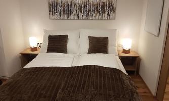 A cozy bedroom with a double bed and wooden floors. On the nightstands are two lamps, and a modern piece of art hangs on the wall.