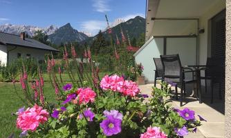 A beautiful garden with colorful flowers and a view of the mountains. In the background, there is a modern terrace with chairs.