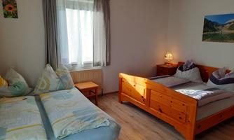 A bright bedroom with two beds and a window through which daylight streams. The walls are decorated with pictures, and there is a cozy atmosphere.