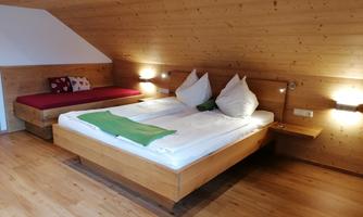 A cozy bedroom with wooden walls and two beds. The bedding is white and there is a green blanket on the bed.