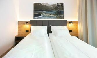 A modern bedroom with two single beds and a painting above the headboard. The warm wooden accents and soft lighting create a cozy atmosphere.