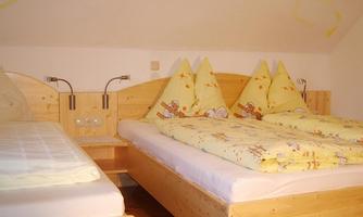 A cozy bedroom with two wooden beds. The bedding has a cheerful pattern and the walls are painted in a light color.