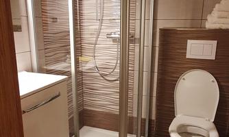 A modern bathroom with a glass shower and a toilet. The floor is decorated with a towel that has the inscription "BATH."