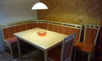 A cozy dining area with a rectangular table and a bench, surrounded by chairs. The walls are made of wood, and a pendant light provides warm light.