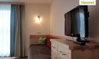 A cozy room with a television and a sofa. Curtains in different colors hang in front of the window.