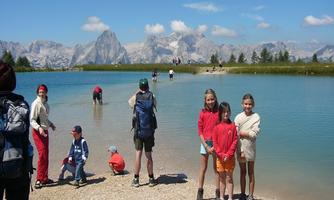 A beautiful day at the lake with families and children playing in the water. In the background, impressive mountains and a clear blue sky can be seen.