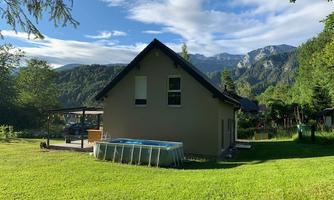 A modern house in a green environment with mountains in the background. A swimming pool is in the garden and the sun is shining.