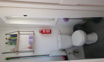 A small bathroom with a toilet, a sink, and shelves. There are cleaning supplies and a fire extinguisher on the shelves.