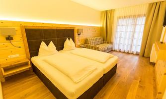 A cozy hotel room with a double bed and two pillows. The wooden paneling and daylight create an inviting atmosphere.
