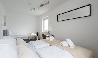 A bright bedroom with two beds, neutral color scheme, and minimalist design. There is a desk with a chair and a large mirror on the wall.