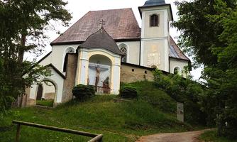 An impressive church sits on a small hill, surrounded by trees. The path to the church is lined with green grass and earth.