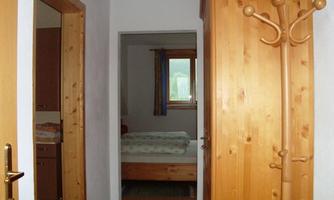 A bright hallway view with wooden doors and a coat rack. In the background, a bedroom with a window is visible.