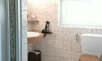 A modern bathroom with a sink, a toilet, and a hairdryer. The walls are designed with gray tiles and there is plenty of natural light.