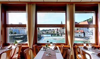 A cozy restaurant with tables and chairs. Behind the windows is a picturesque view of a river and the city.