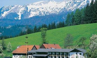 A picturesque hotel in a green landscape, surrounded by impressive snow-capped mountains. The clear sky and natural elements create an inviting atmosphere.