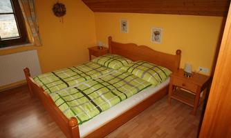 A cozy bedroom with a double bed and yellow walls. Next to the bed are two nightstands with lamps.