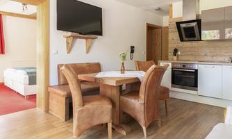 A cozy vacation apartment with a dining table and chairs made of leather. The modern kitchen is well-equipped, and a TV is mounted on the wall.