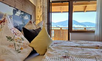 A cozy bedroom with comfortable beds and decorative cushions. The large windows provide a beautiful view of the mountains.