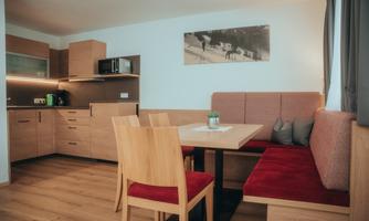 A modern kitchen with wooden cabinets and a cozy dining area. The table is decorated with a small plant, and there are red chairs.