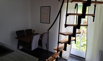 A modern room with a spiral staircase and a small dining area. Large windows let in plenty of daylight.