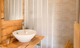 A modern bathroom with a shower unit and a sink on a wooden shelf. Clean towels in various colors are neatly arranged.