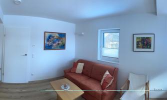 A bright and modern apartment with an open living area. The space includes a seating area with a red sofa and a kitchenette.