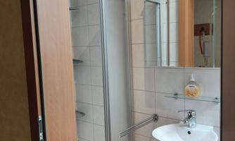 A modern bathroom with a shower and sink. The walls are tiled in light colors and there is a large mirror.