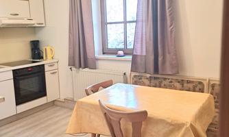 A cozy kitchen corner with a round table and chairs. The room is bright and has a window with a view outside.