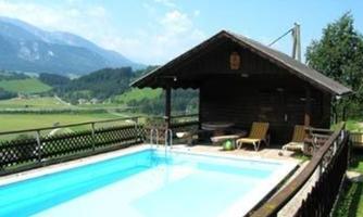 A cozy wooden house with a pool in a picturesque landscape. In the background, green hills and mountains are visible.