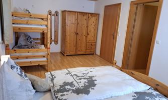 A bright bedroom with a bunk bed and a large double bed. The room has wooden furniture and an inviting atmosphere.