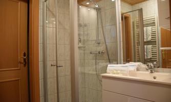 A modern bathroom with a glass shower cabin and a white sink. The walls are tiled and there is ample lighting.
