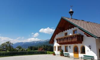 A beautiful traditional house in the mountains with a clear blue sky. In the background, the snow-capped peaks and green meadows can be seen.