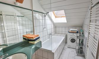 A modern bathroom with a bathtub, a sink, and a washing machine. The room is bright and well-organized, with towels on a shelf.