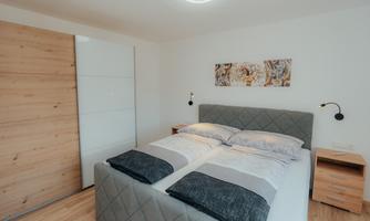 A modern bedroom with a cozy double bed and wooden furniture. The walls are painted bright, and a piece of artwork gives the room character.