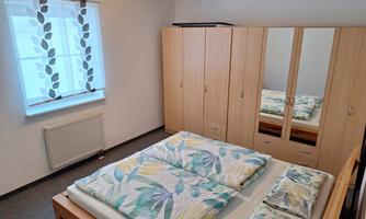 A cozy bedroom with a double bed and colorful bedding. The walls are bright and a wardrobe with mirrors is in the room.