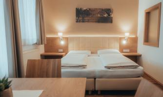 A cozy bedroom with two beds and wooden decor. Bright curtains and soft lighting create a relaxed atmosphere.