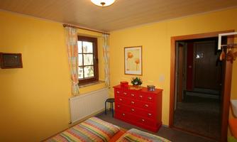 A colorful bedroom with yellow walls and a red dresser. The beds are adorned with striped bedding and a window provides daylight.