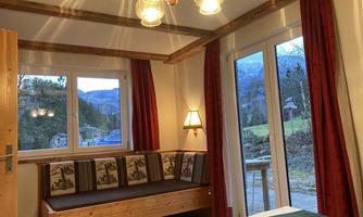 A bright room with wooden details and a cozy corner sofa. Large windows offer a view of the surrounding landscape.