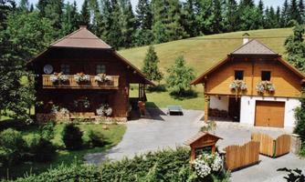 Two pretty wooden houses surrounded by green trees and meadows. The garden is well maintained and adorned with flowers.