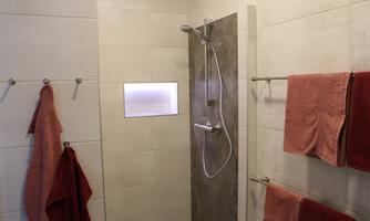 A modern shower with gray tiles and pink towels. Red towels hang on the wall, and a small window opening provides light.