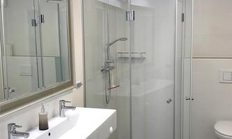 A modern bathroom with a glass shower and a double sink. The room has bright walls and a wooden floor.