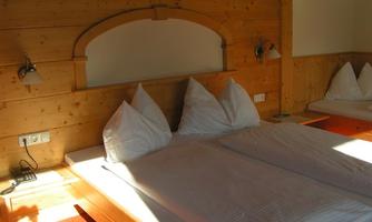 A cozy bedroom with wood paneling and two beds. The bedding is light and tidy, and there is an additional single bed in the background.