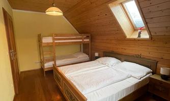 A cozy bedroom with wooden paneling. There is a double bed and a bunk bed, as well as a window that lets in natural light.