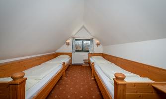 A simple room with two wooden single beds. The roof is slanted and a window provides daylight.