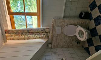 A simple bathroom with a toilet and a window. The floor features a simple, multicolored pattern.