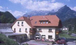 A cozy house with red tiled roofs, surrounded by mountains. The sky is clear with some clouds.