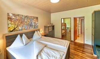 A cozy bedroom with a large double bed and two pillows. On the wall hangs a picture of an autumn tree.