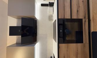 A modern kitchen with wooden cabinets and an elegant cooking island. The wall is equipped with a black hood.